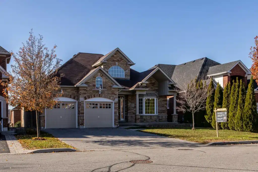 A two-story brick house with a double garage, arched windows, and a neatly kept lawn under a clear blue sky.